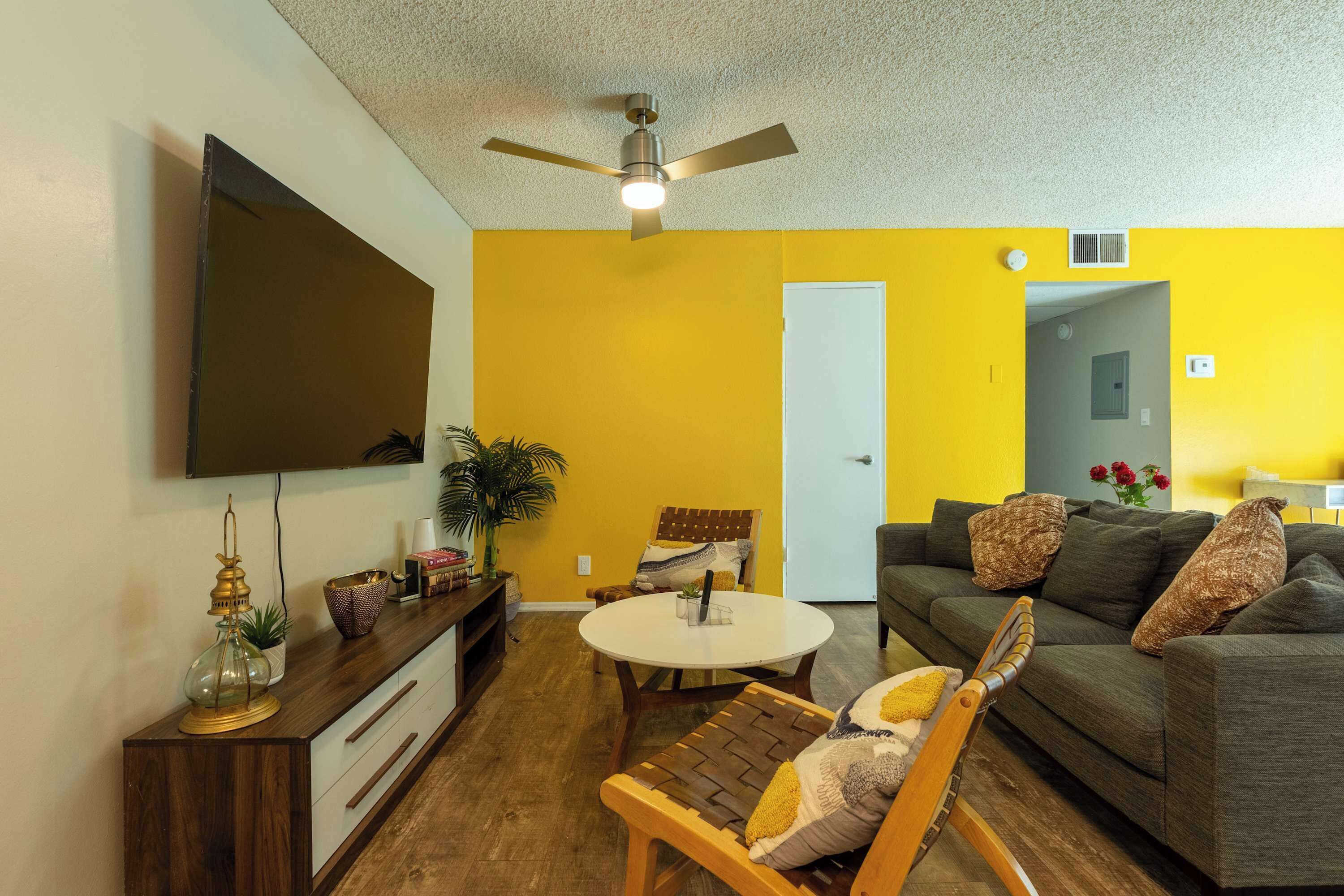 A living room with a ceiling fan, a flat-screen TV, a round coffee table, a sofa, and a wooden chair.