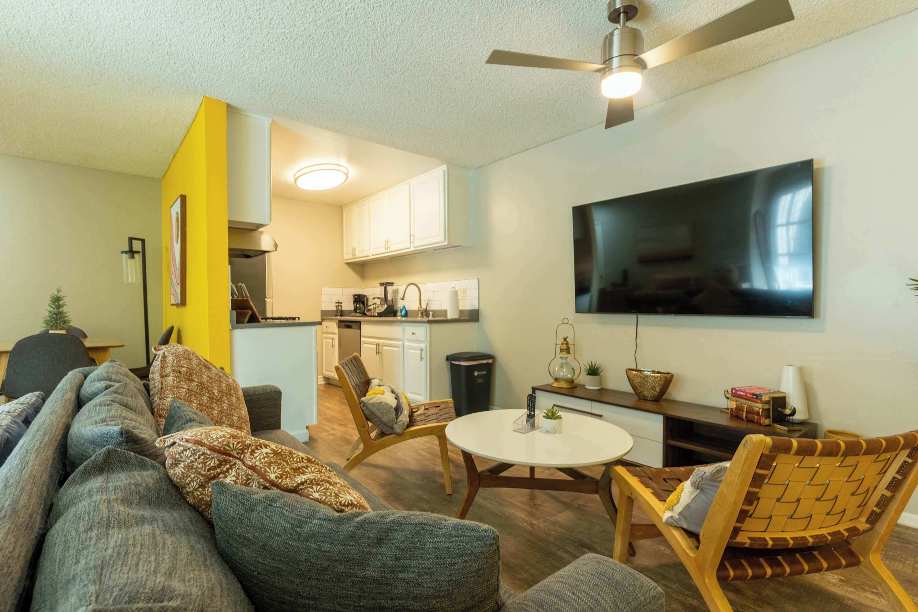 A modern living room with a sofa, chairs, a dining table, and a kitchen in the background.
