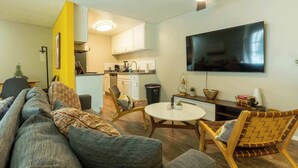 Ein modernes Wohnzimmer mit einer Couch, Sesseln, einem Esstisch und einer Küche im Hintergrund.