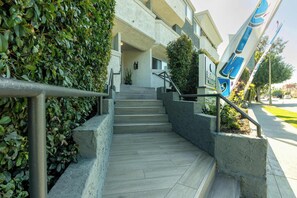 A staircase leading to a building entrance with a metal handrail, concrete steps, and a hedge on the left. - Sleek And Chic Getaway (Beverly Hills)