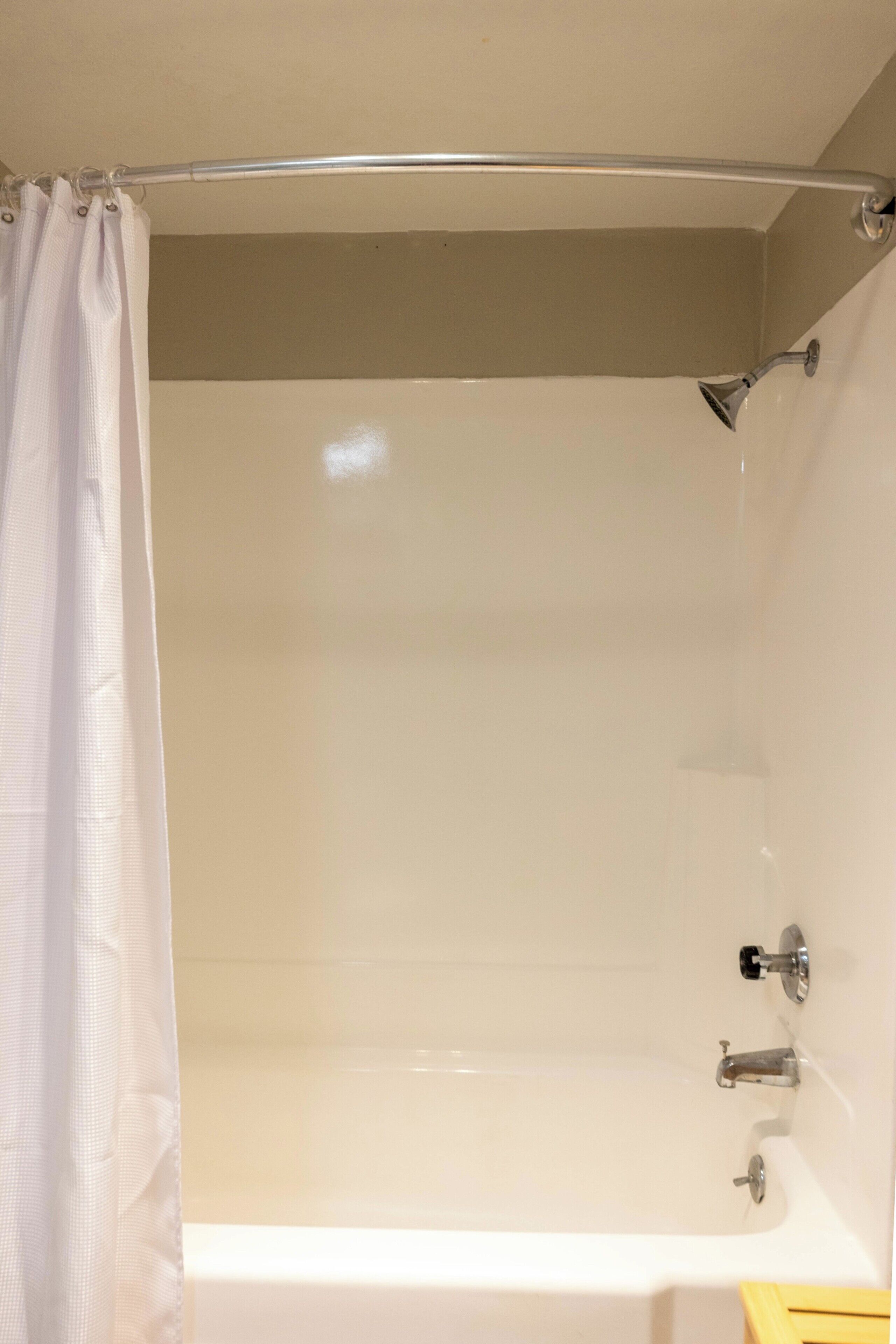 A bathtub with a showerhead, a curtain, and a faucet.