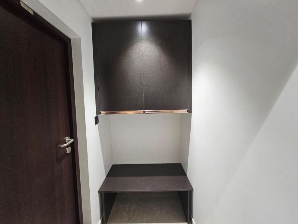 Une pièce avec une porte sombre, un mur blanc et un meuble sombre doté d’une étagère.