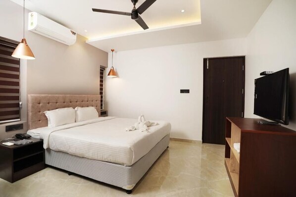 A modern bedroom with a bed, ceiling fan, TV, and a wooden nightstand. - 7 The Business Hotel (Aluva)