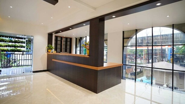 A reception desk with a dark wood finish, a glass partition, and a view of the street outside. - 7 The Business Hotel (Aluva)