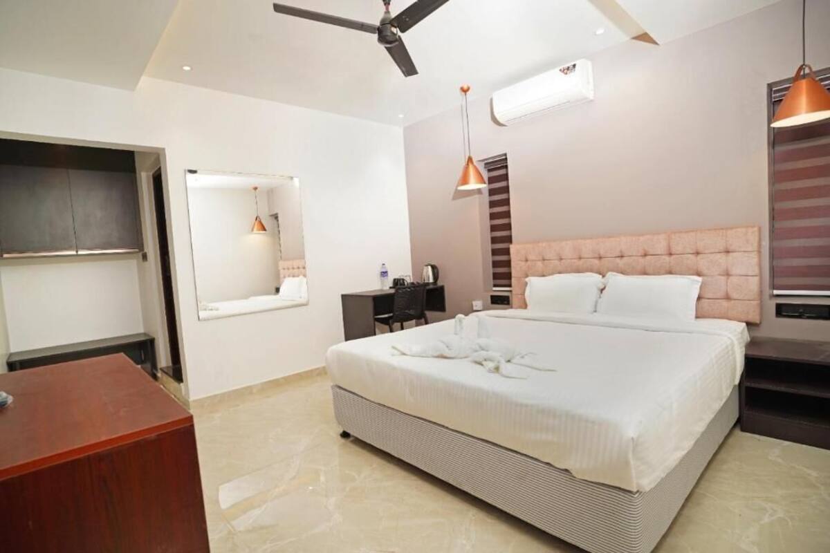 A bedroom with a bed, a desk, a chair, a ceiling fan, and a hanging light fixture.