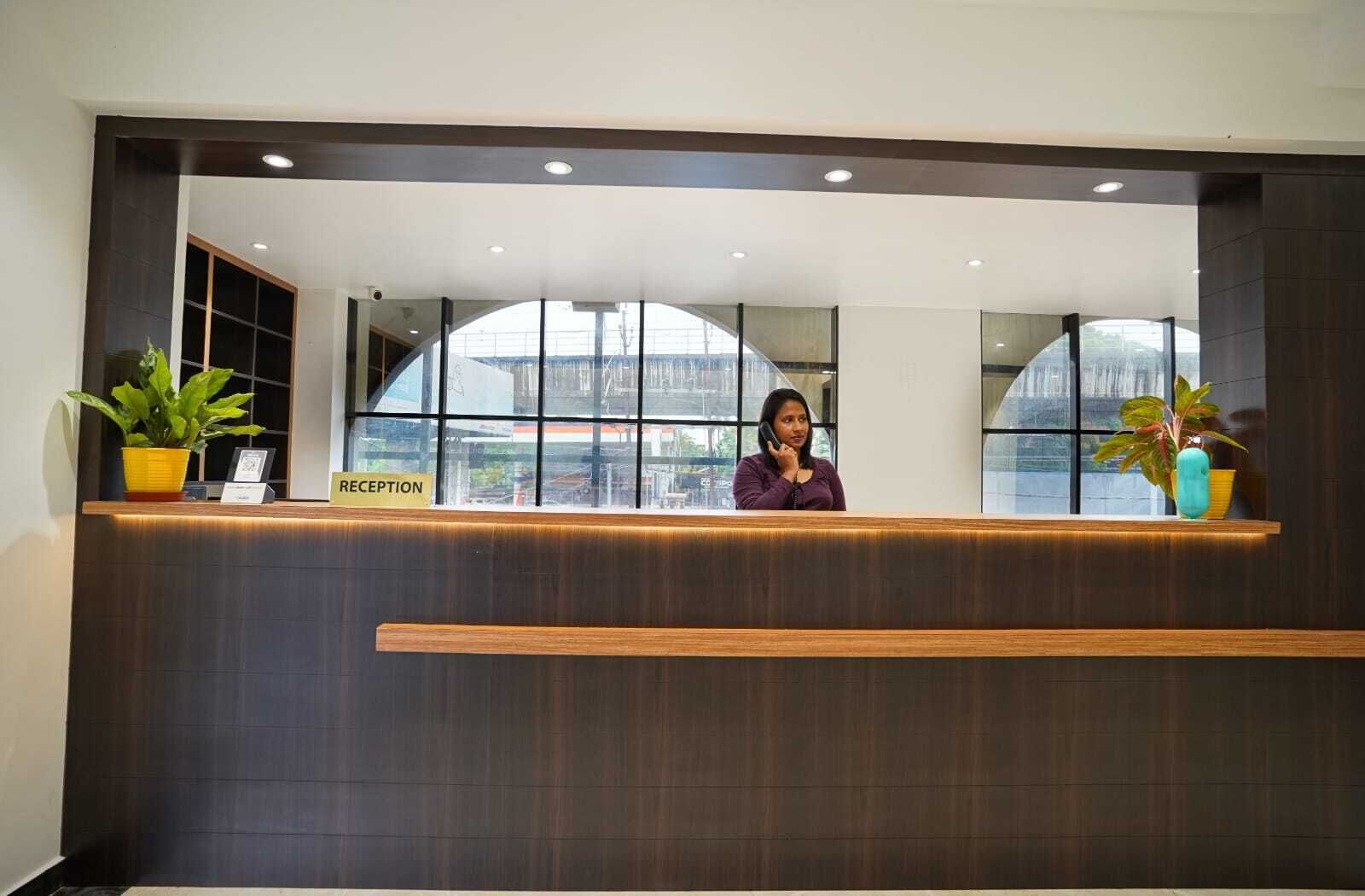 A reception desk with a 'RECEPTION' sign, a receptionist, and large windows with a view.