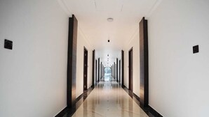 A long, narrow hallway with a polished floor and dark vertical accents on the walls. - 7 The Business Hotel (Aluva)
