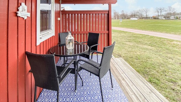 A red building with a covered porch, a table with chairs, and a lantern.