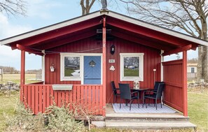 Une petite cabane rouge avec une véranda, deux fenêtres et une porte.