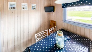 A room with wooden walls, a television mounted on the wall, a window with a view of a grassy area, and a table with a star-patterned tablecloth.