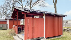 A red wooden structure with a porch and a covered area, surrounded by a grassy area and trees.