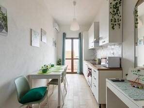 A compact kitchen with a dining area, a microwave, a sink, and a small table with chairs. - Appartamento con Aria Condizionata (Trinità d'Agultu e Vignola)