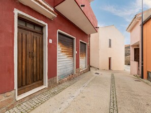 A narrow alleyway with a red building on the left, a beige building on the right, and a cobblestone path. - Appartamento con Aria Condizionata (Trinità d'Agultu e Vignola)