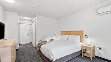 A hotel room with a bed, bedside table, lamp, and a desk with a chair.