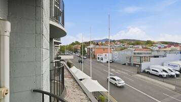 A street view with a building featuring a balcony, a road with cars, and a sign for 'birchalls.'