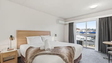 A hotel room with a large bed, a bedside table, a lamp, a chair, and a view of the city through the window.