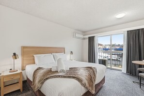 Ein Hotelzimmer mit einem großen Bett, einem Nachttisch, einer Lampe, einem Sessel und Blick auf die Stadt durch das Fenster.