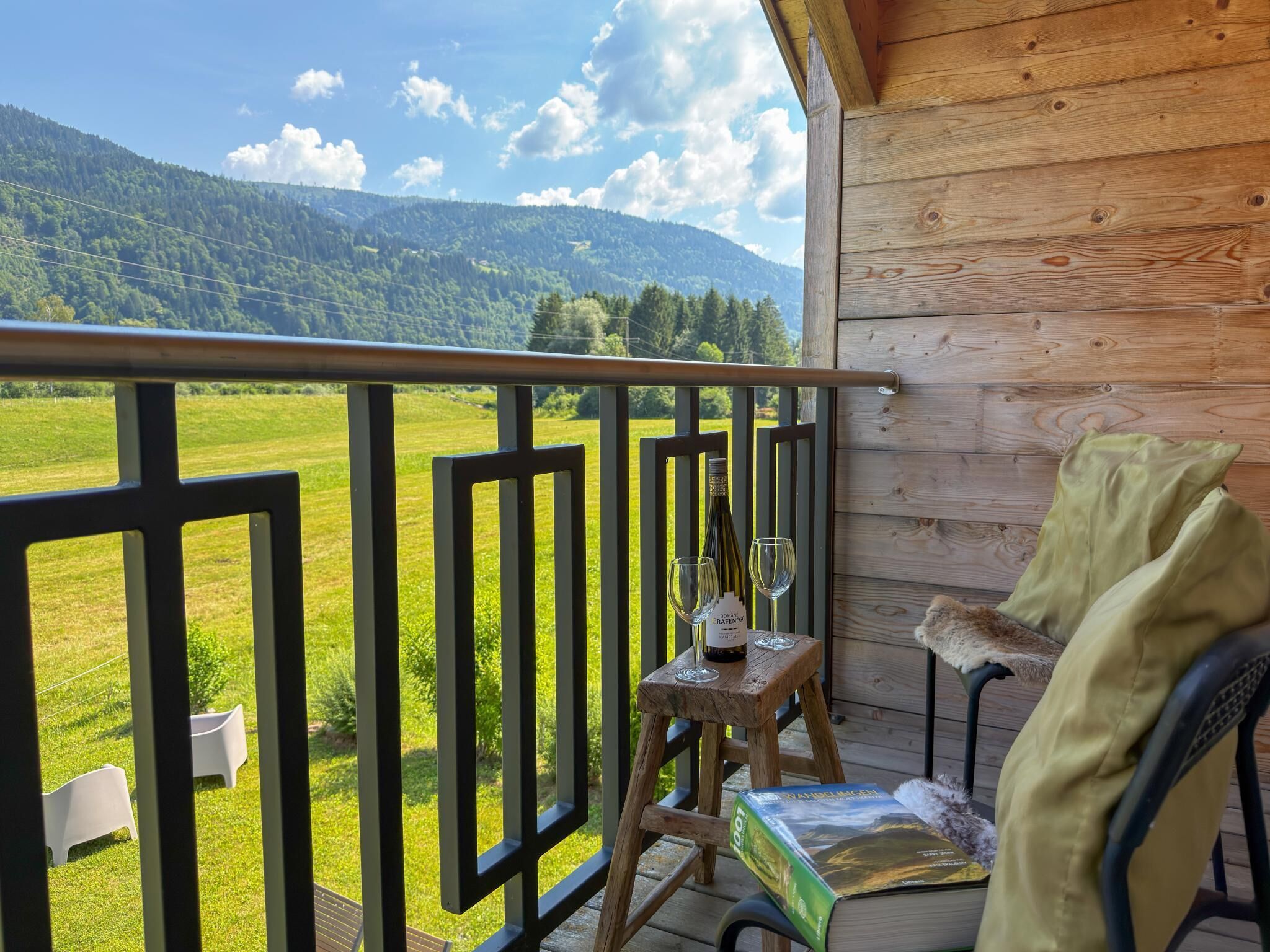 Een houten balkon met uitzicht op een groen veld en bergen.