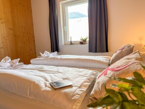 A hotel room with two beds, a window with curtains, a small table with a plant, and a view of mountains. - Cosy apartment near ski area Nassfeld (Rattendorf)