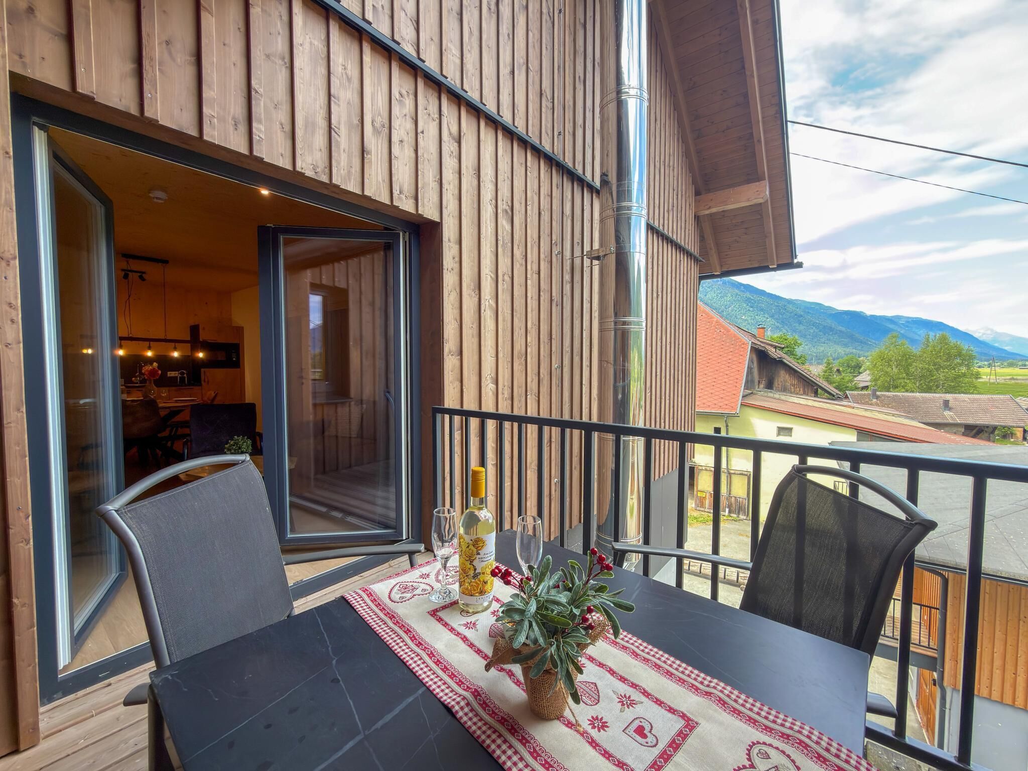 A balcony with a table set for two, a potted plant, and a bottle of wine.