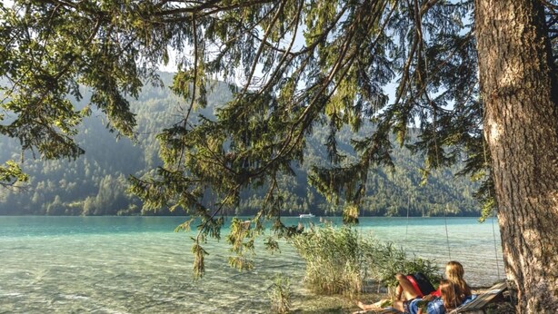 Un lago con acque cristalline, circondato da alberi e una barca con due persone.