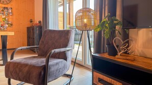 Un soggiorno moderno con una poltrona imbottita marrone, una lampada da terra, un televisore e un mobile contenitore in legno.