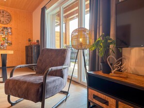 En moderne stue med en brun polstret stol, en gulvlampe, et fjernsyn og et træskab.