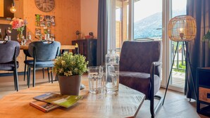 Una stanza accogliente con soffitto in legno, una zona pranzo con sedie e tavolo, un'ampia finestra con tende e vista sull'esterno.