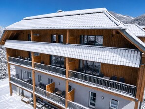 En flerretagers træbygning med altaner, store vinduer og et sneklædt landskab.