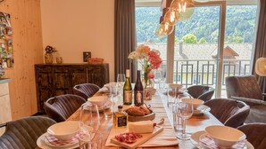 Una tavola imbandita con piatti, bicchieri e una bottiglia di vino, con vista sull'esterno attraverso ampie finestre.