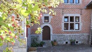 En traditionel murbygning med stensokkel, en midtertilmuret buet indgang og en lille gårdhave med plantekasser.