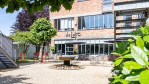 Een binnenplaats met een fontein, zitplaatsen buiten, en een gebouw met grote ramen en een bord waarop 'de l'ort' staat.