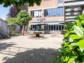 Un patio con una fuente, asientos al aire libre y un edificio con ventanas amplias y un letrero que dice 'de l'ort'.