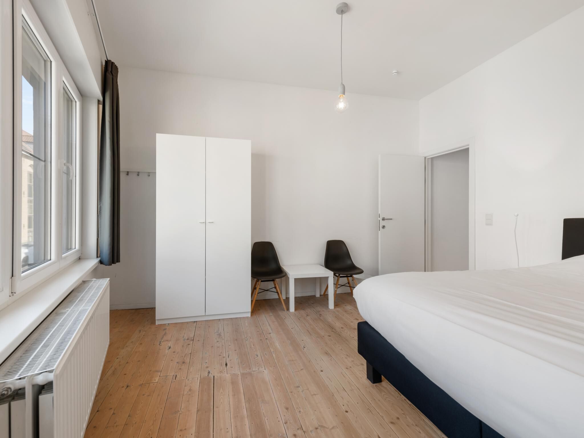 A bedroom with a bed, a wardrobe, a desk, two chairs, and a radiator.