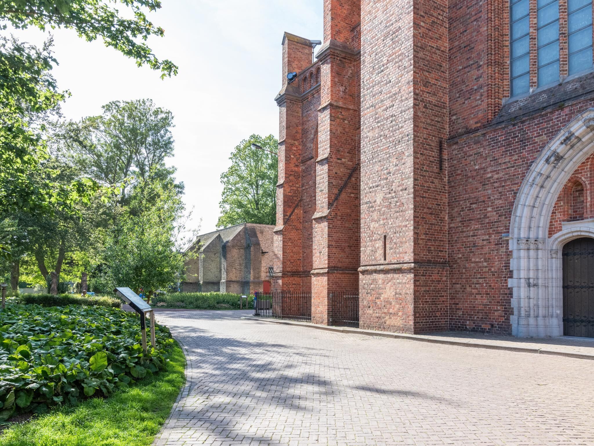 A brick building with a large arched entrance, a paved pathway, and greenery.