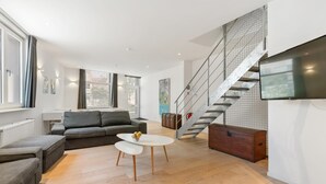 Een moderne woonkamer met een grijze bank, een witte salontafel en een trap met een metalen leuning.