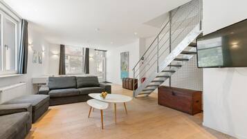 Un salon moderne avec un canapé gris, une table basse blanche et un escalier doté d’une rampe en métal.