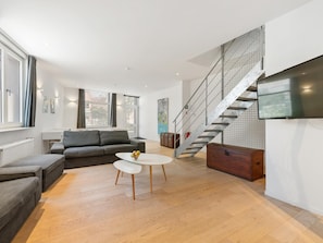 Una sala de estar moderna con sofá, mesa de centro y una escalera, además de un televisor.