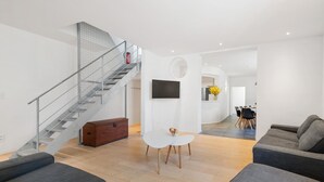 Een moderne woonkamer met een trap, grijze banken, een witte salontafel en een flatscreen televisie aan de muur.