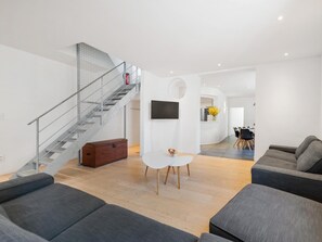 Ein modernes Wohnzimmer mit Treppe, grauen Sofas, einem weißen Couchtisch und einem an der Wand befestigten Flachbildfernseher.