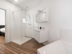 Un baño moderno con cabina de ducha de vidrio, un lavamanos blanco con espejo encima y suelo de madera.