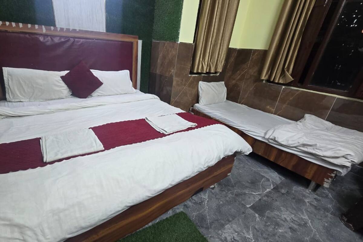 A double bed with a wooden headboard, a smaller single bed, and a red accent pillow.