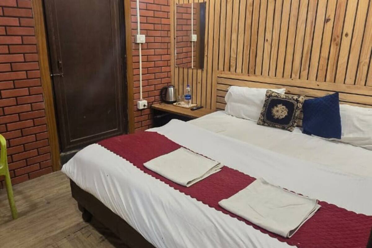 A bedroom with a wooden slat wall, a brick wall, a wooden floor, a bed with white bedding, a nightstand, a lamp, and a door.