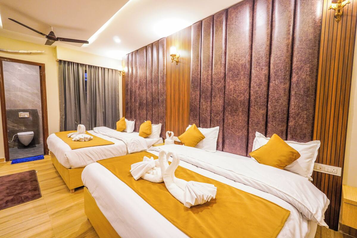 A hotel room with two beds, a ceiling fan, a bathroom with a toilet and sink, and a large window with curtains.