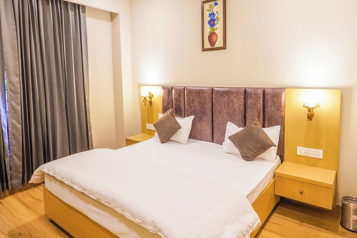 A bedroom with a bed, a ceiling fan, a nightstand, a wall-mounted light, and a curtain.