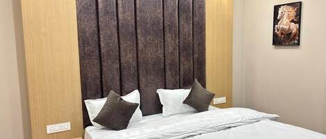 A hotel room with a bed, a headboard, a nightstand, and a wall-mounted light fixture.