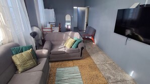 Een woonkamer met een bank, fauteuils, een televisie en een ventilator.