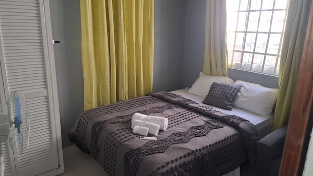Een slaapkamer met een bed, gordijnen, een raam en een ventilator.
