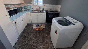 Een kleine keuken met witte kastjes, een magnetron, een fornuis en een wasmachine.