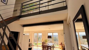 A spacious interior with a wooden floor, a dining area, a staircase, and a view through large windows. - Far-reaching views of the Mangfall valley - Quiet house with sauna, hot tub & garden near Munich (Feldkirchen-Westerham)